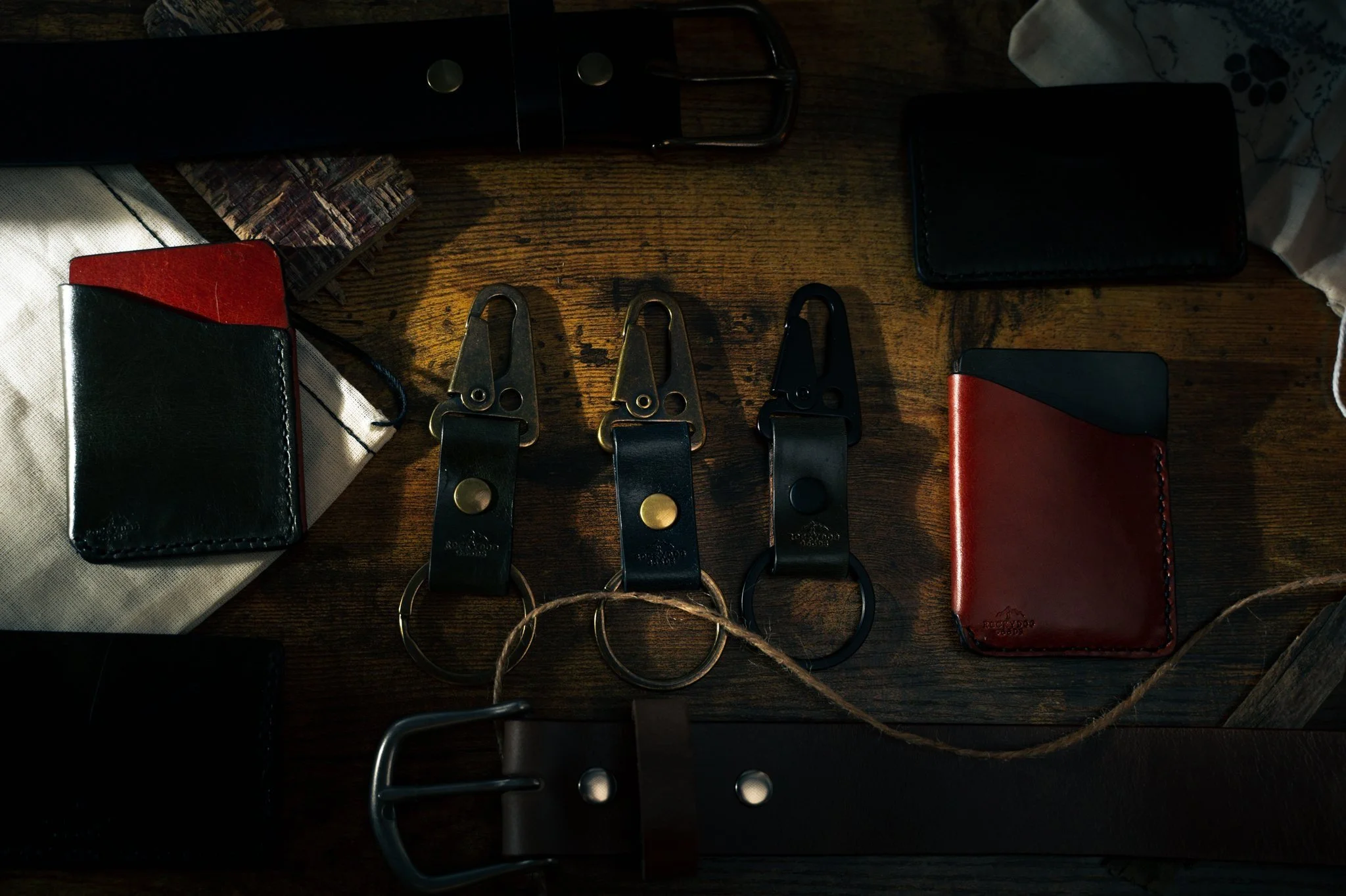 Wallets, hook fobs, and belts laid out together on a dark wood workbench