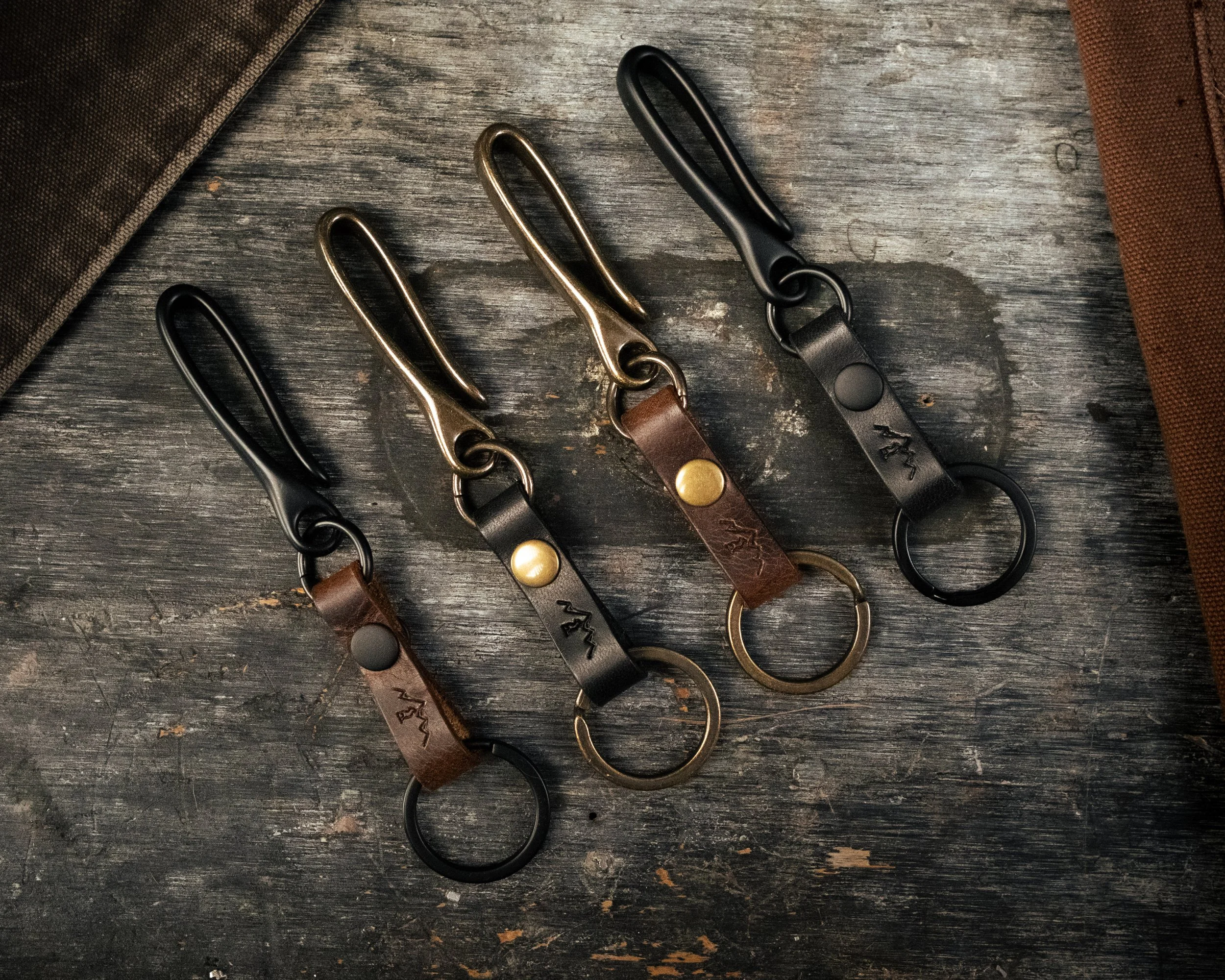Leather hook fobs in brown and black with brass hardware, laid on weathered wood